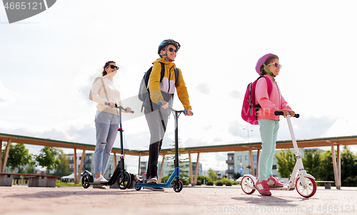 Image of happy school children with mother riding scooters