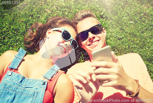 Image of happy teenage couple smartphone lying on grass