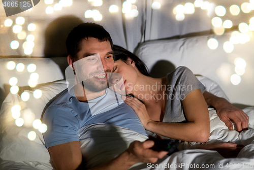 Image of happy couple watching tv in bed at night at home