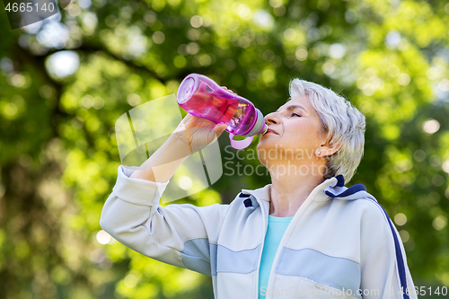 Image of senior woman drinks water after exercising in park