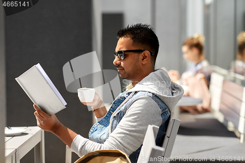 Image of man reading book and drinking coffee at city cafe