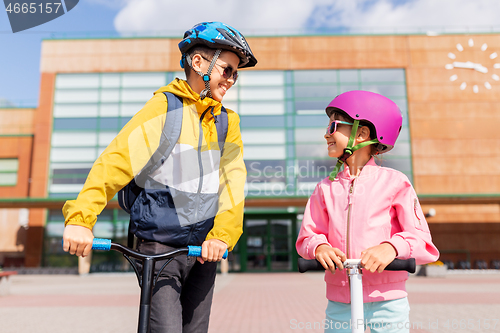 Image of happy school children in helmets riding scooters