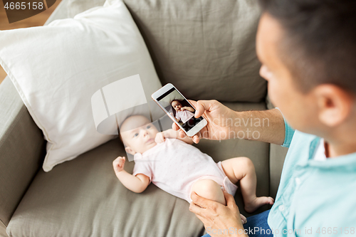 Image of father with smartphone taking picture baby at home