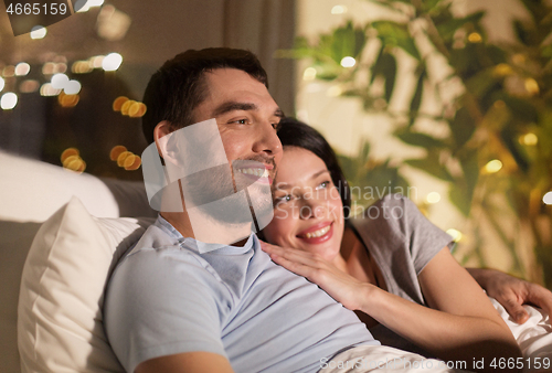 Image of happy couple watching tv in bed at night at home