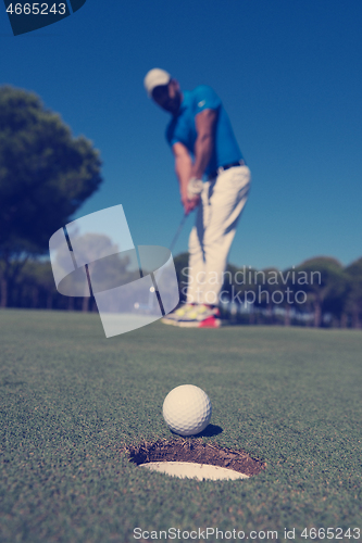 Image of golf player hitting shot, ball on edge of hole