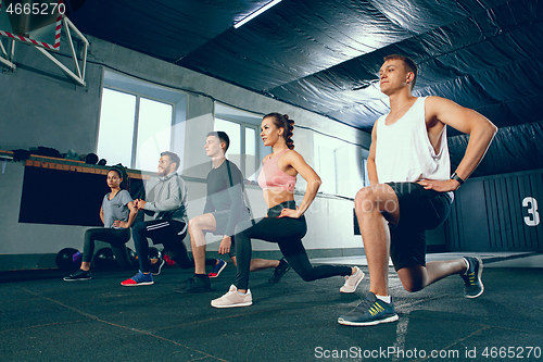 Image of Shot of young men and a woman standing in plank position at the gym