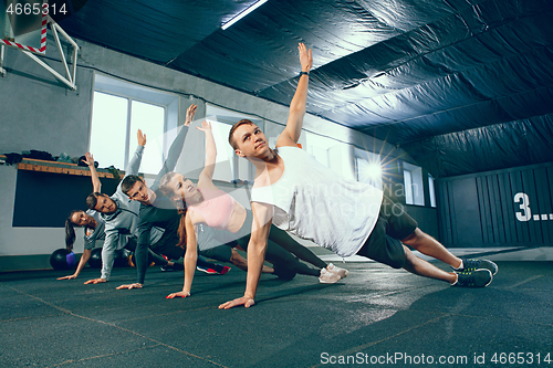 Image of Shot of young men and a woman standing in plank position at the gym