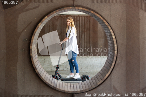 Image of Casual caucasian teenager riding urban electric scooter in urban environment. Urban mobility concept