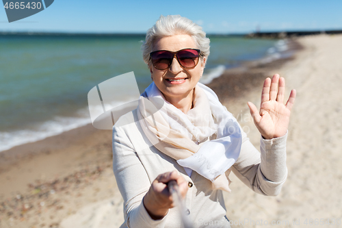 Image of old woman taking selfie and waving hand on beach