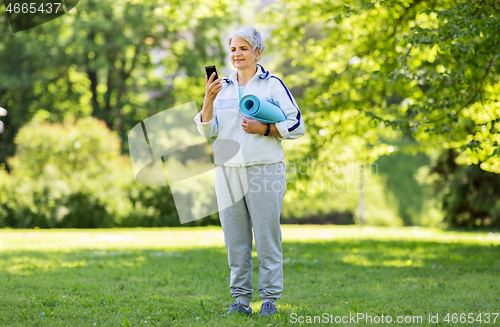 Image of old woman with exercise mat and smartphone at park