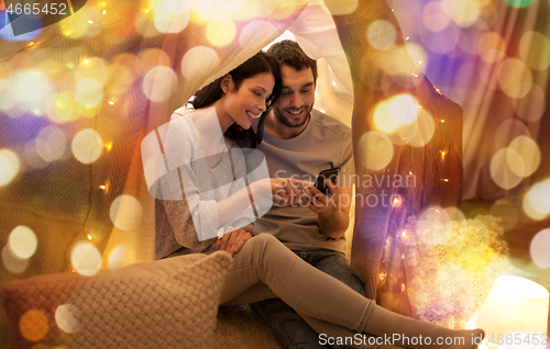 Image of happy couple with smartphone in kids tent at home