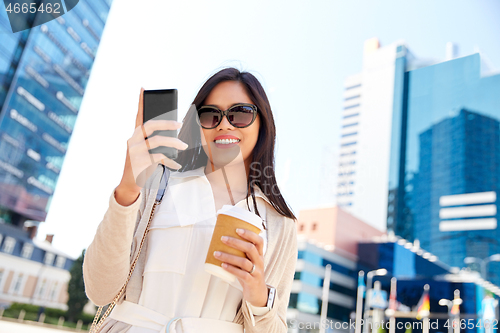 Image of smiling woman with smartphone and coffee in city