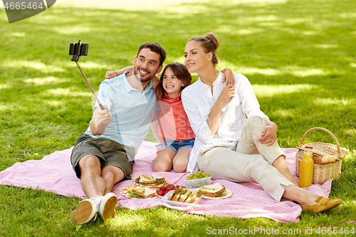 Image of family having picnic and taking selfie at park