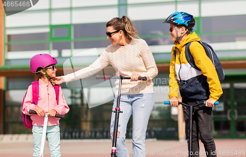 Image of happy school children with mother riding scooters