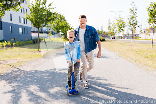 Image of happy father and little son riding scooter in city