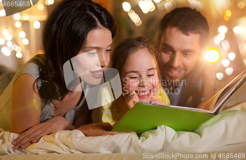 Image of happy family reading book in bed at night at home