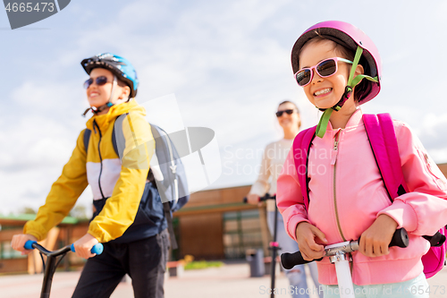 Image of happy school children with mother riding scooters