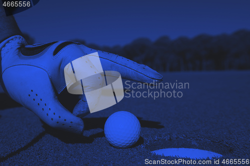 Image of man\'s hand putting golf ball in hole