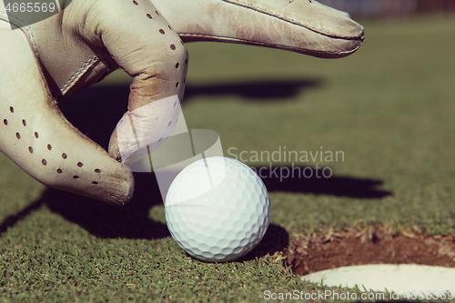 Image of man\'s hand putting golf ball in hole