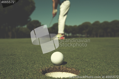 Image of golf player hitting shot, ball on edge of hole