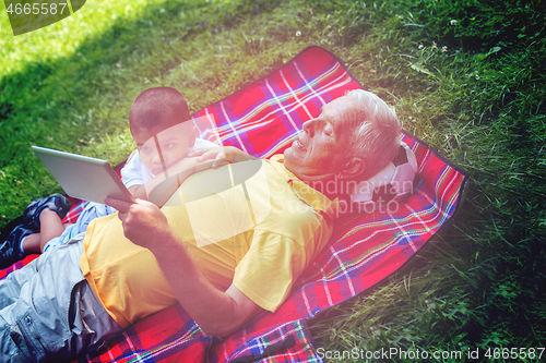 Image of grandfather and child in park using tablet