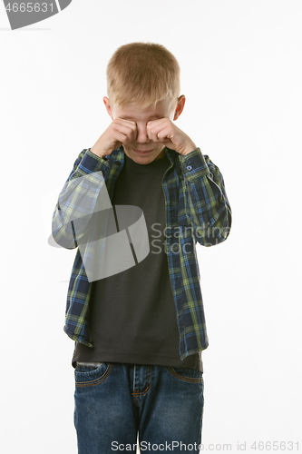 Image of Crying boy rubs his eyes with his fists