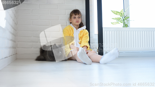 Image of An upset girl in a yellow bathrobe sits in the corner of the room, a dark gray domestic cat sits nearby