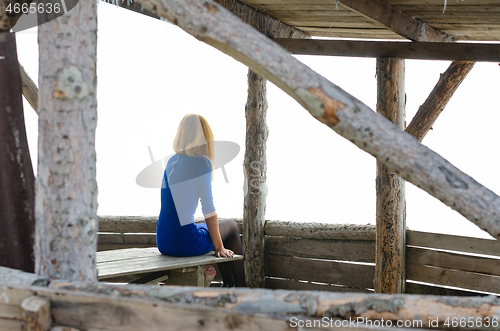 Image of A girl sits on a table in a gazebo from a log house