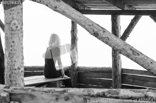 Image of Girl alone sits early in the morning on a foggy day in a wooden arbor