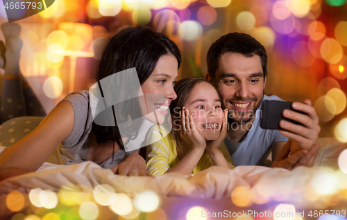 Image of happy family with smartphone in bed at night