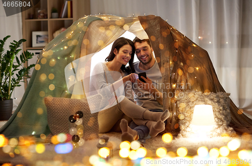 Image of happy couple with smartphone in kids tent at home