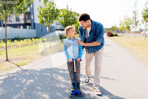 Image of happy father and little son riding scooter in city