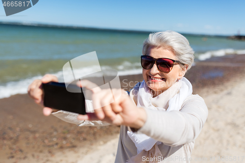 Image of senior woman taking selfie by smartphone on beach