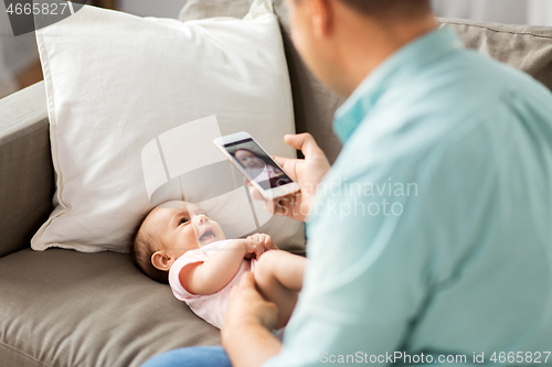 Image of father with smartphone taking picture baby at home