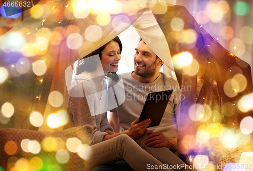 Image of happy couple with tablet pc in kids tent at home