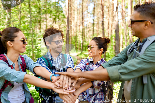 Image of friends with backpacks stacking hands in forest