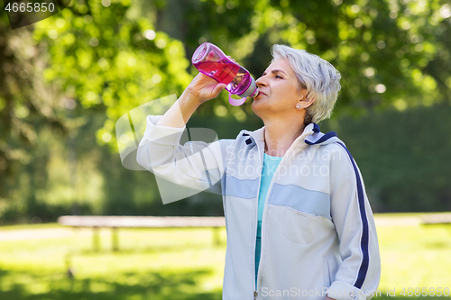 Image of senior woman drinks water after exercising in park