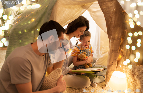 Image of happy family reading book in kids tent at home