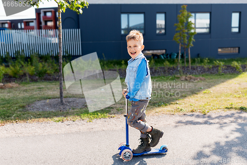 Image of happy little boy riding scooter in city