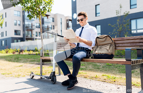 Image of businessman with scooter reading newspaper in city