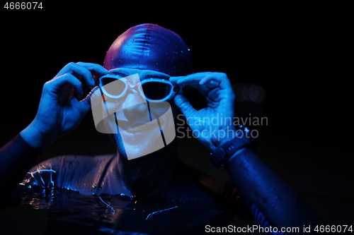 Image of authentic triathlete swimmer having a break during hard training on night neon gel light