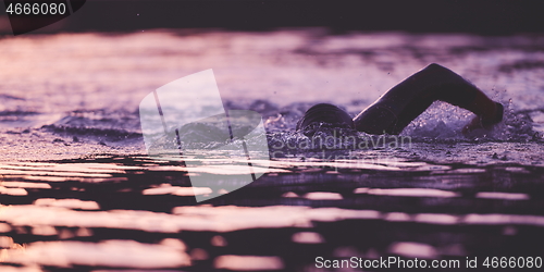 Image of triathlon athlete swimming on lake in sunrise wearing wetsuit