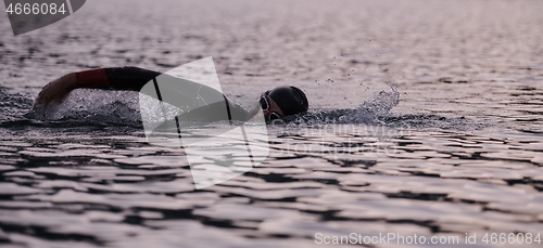 Image of triathlon athlete swimming on lake in sunrise wearing wetsuit