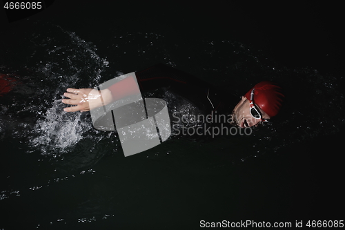 Image of triathlon athlete swimming in dark night wearing wetsuit