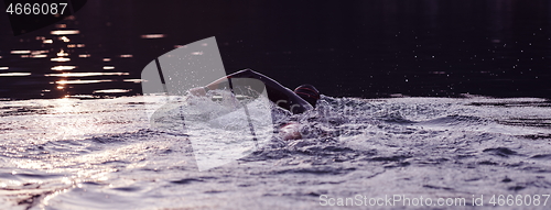 Image of triathlon athlete swimming on lake in sunrise wearing wetsuit