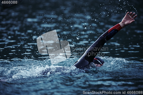 Image of triathlon athlete swimming on lake in sunrise wearing wetsuit