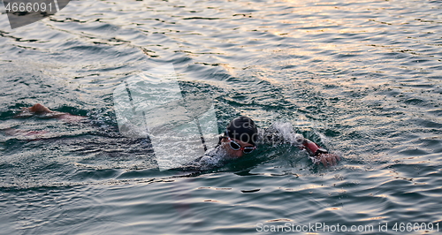 Image of triathlon athlete swimming on lake in sunrise wearing wetsuit