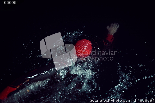 Image of triathlon athlete swimming in dark night wearing wetsuit