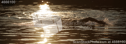 Image of triathlon athlete swimming on lake in sunrise wearing wetsuit