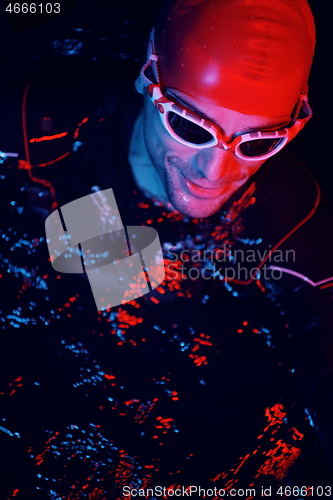 Image of authentic triathlete swimmer having a break during hard training on night neon gel light